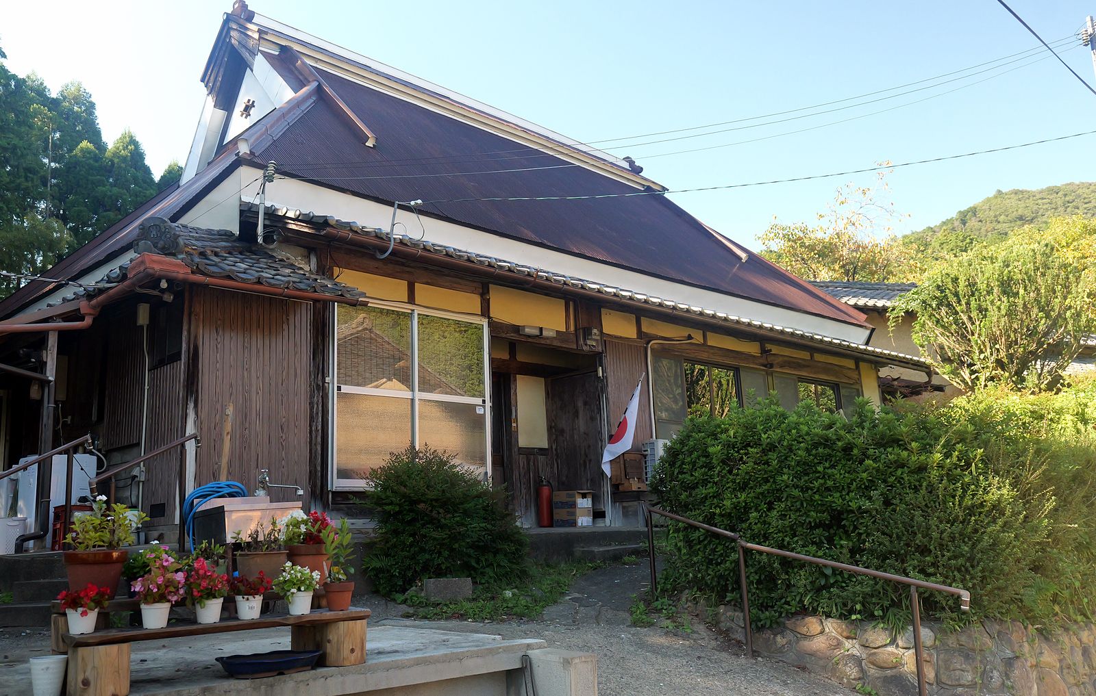 急な勾配の大屋根をもつ平屋の古民家。軒先に花の鉢が並ぶ